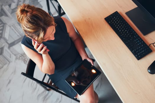 Businesswoman having business call working on tablet in office. Mature busy woman using touch pad computer standing by window in modern interior. Female manager focused on work holding digital device. Using technology