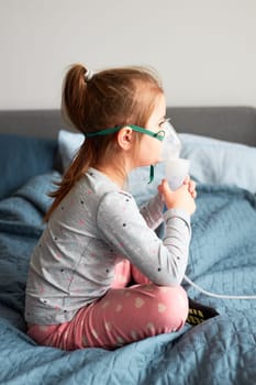 Sick little girl having medical inhalation treatment with nebuliser. Child with breathing mask on her face sitting in bed