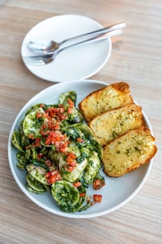 Clam Pesto Salsa in a round white plate, next to an empty plate and cutlery, on a wood grain table, natural light. Selective focus.