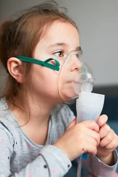 Sick little girl having medical inhalation treatment with nebuliser. Child with breathing mask on her face sitting in bed