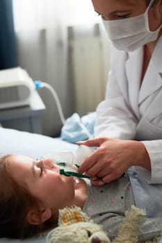 Doctor visiting little patient at home. Child having medical inhalation treatment with nebuliser. Girl with breathing mask on her face. Woman wearing uniform and face mask