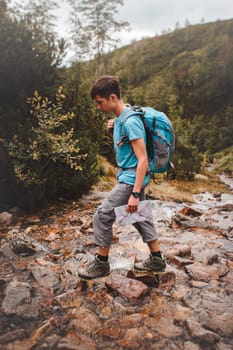 Boy with backpack going across a mountain stream during hiking in mountains