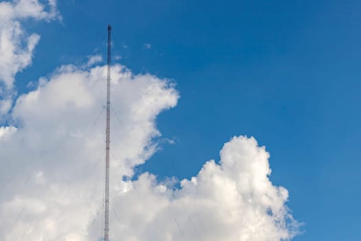 A radio antenna made of steel frame sits on the left side of the image, with a sling attached to the ground. The background is a bright blue sky with white clouds. There is a copy space on the right s