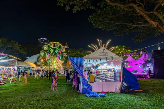 Bangkok, Thailand - Dec 8, 2022 : Crowds of people walk into a beautifully lit amusement park during the Red Cross Fair to be held from December 8-18, 2022. The image is blurred by the movement.