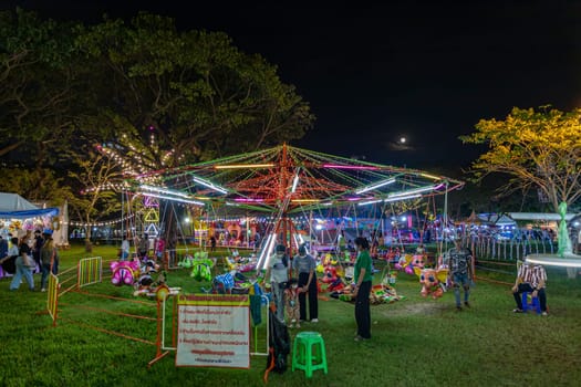 Bangkok, Thailand - Dec 8, 2022 : Crowds of people walk into a beautifully lit amusement park during the Red Cross Fair to be held from December 8-18, 2022. The image is blurred by the movement.