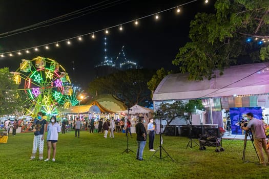 Bangkok,Thailand - Dec 8, 2022: A local reporter is reporting with a Ferris wheel in the background. during the Red Cross Fair to be held from December 8-18, 2022. The image is blurred by the movement