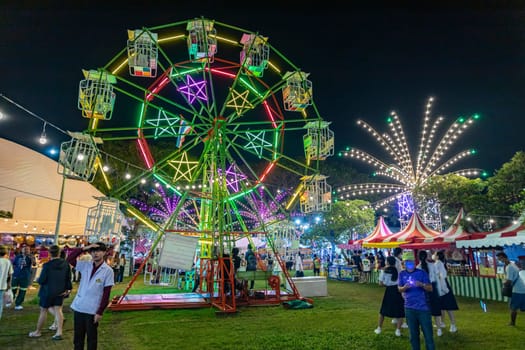 Bangkok, Thailand - Dec 8, 2022 : Crowds of people walk into a beautifully lit amusement park during the Red Cross Fair to be held from December 8-18, 2022. The image is blurred by the movement.