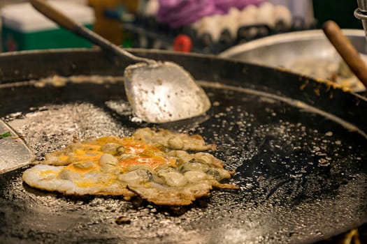 Oysters fried while on a hot black pan Asian style circle and spatula, a delicious Thai dish made with oysters, flour, eggs and fried until crispy. famous thai food called Hoy-Tod. Selective focus.