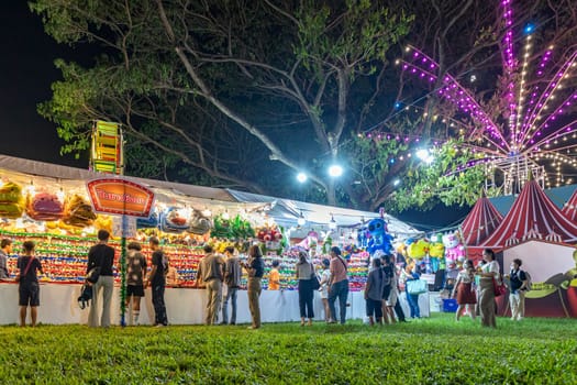 Bangkok, Thailand - Dec 8, 2022: Visitors to the Red Cross Fair at Lumpini Park, held from December 8-18, 2022, are shooting airsoft rifles to win colorful dolls. ฺBeautiful lights. Motion blur.