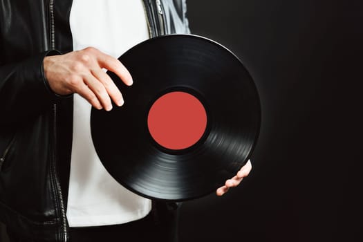 Man with vinyl record. Vintage music style. Rock style. Male wearing black jacket holding turntable plate standing on black background. Retro music. Classic audio. Copy space right