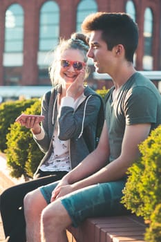 Couple of friends, teenage girl and boy,  having fun together with smartphones,  sitting in center of town, spending time together