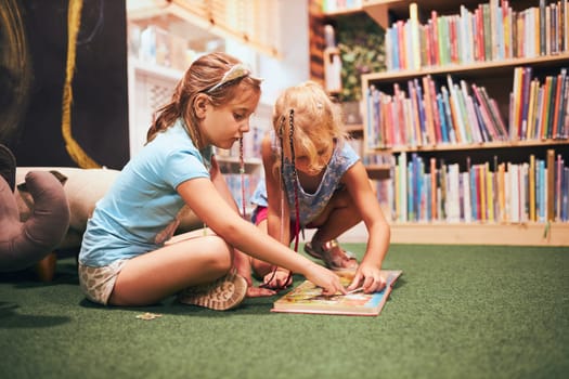 Two elementary schoolgirls solving puzzles and riddles in school library. Students learning from books. Pupils having fun in library. Back to school