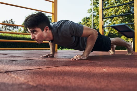 Young man doing push-ups on a red rubber ground during his workout in a modern calisthenics street workout park. Man wearing sportswear looking away