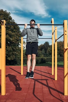 Young man doing pull-ups on pull-up horizontal bar during his workout in a modern calisthenics street workout park. Man wearing sportswear