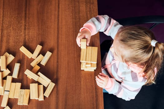 Little girl preschooler playing with wooden blocks toy building a tower. Concept of building a house