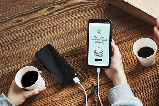 Online shopping. Buying online. Ordering product in online shop using smartphone. Order confirmation on screen. Online banking. People paying online. Paying for online shopping while charging mobile phone from powerbank in coffee shop