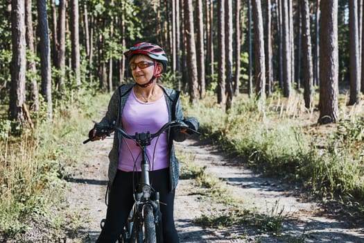 Active woman cycling on forest road. Female riding bicycle off-road route on summer vacation day. Woman wearing bicycle helmet and gloves