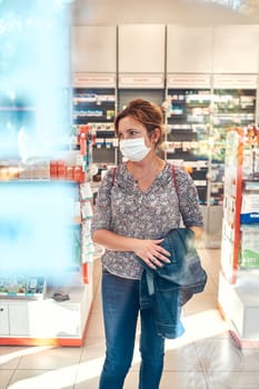 Woman shopping at pharmacy, buying medicines, wearing face mask to cover mouth and nose during pandemic coronavirus outbreak