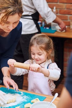 Little girl rolling the dough with her mom's help for the cookies. Cutting the dough to heart shapes. Kid taking part in baking workshop. Baking classes for children, aspiring little chefs. Learning to cook. Combining and stirring prepared ingredients. Real people, authentic situations