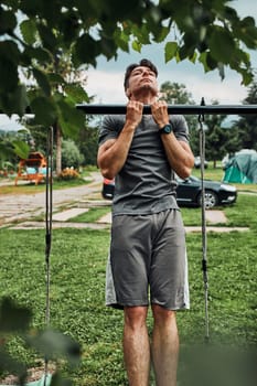 Young man doing pull-ups on pull-up horizontal bar during his calisthenics workout on a camping during his summer vacation trip
