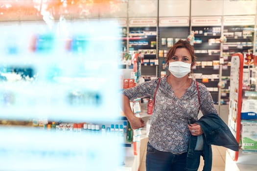 Woman shopping at pharmacy, buying medicines, wearing face mask to cover mouth and nose during pandemic coronavirus outbreak