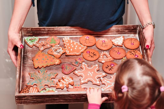 Little girl looking at tray filled with baked Christmas gingerbread cookies in many shapes