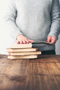 Young woman looking at pages of old book on wooden table in antique bookstore. Woman wearing grey sweater and jeans. Vertical photo. Space for text