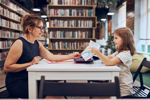 Teacher assisting schoolgirl during art class looking at child drawing. Child doing homework sitting at desk in afterschool club. Girl drawing pictures. Learning at primary school. Elementary education. Back to school