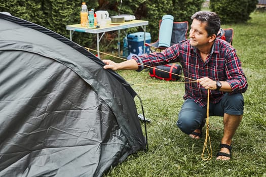 Man putting up a tent at camping during summer vacation. Preparing campsite to rest and relax. Spending vacations outdoors close to nature
