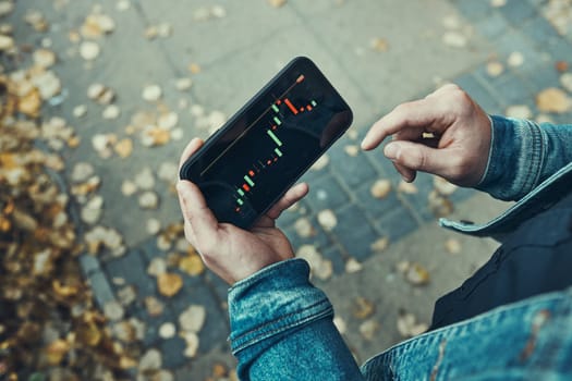 Person investing trading on stock cryptocurrency market using investing application on smartphone. Stock market investment in hand. Trader holding mobile phone looking at candle chart