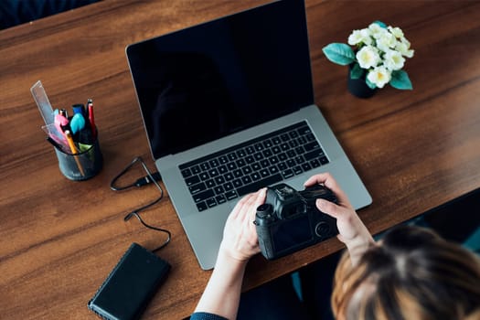 Female photographer working on photos on laptop and camera. Woman editing retouching browsing photos working as a freelancer sitting at desk