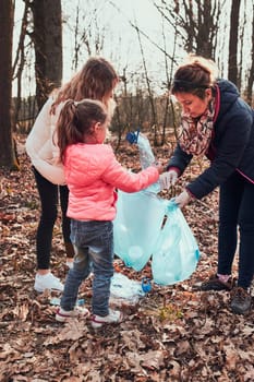 Family cleaning up a forest. Volunteers picking plastic waste to bags. Concept of plastic pollution and too many plastic waste. Environmental issue. Environmental damage. Responsibilitiy for environment. Real people, authentic situations