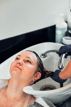 Hairdresser styling dyeing combing womans hair. Young woman working as a hairdresser in hair salon. Real people, authentic situations