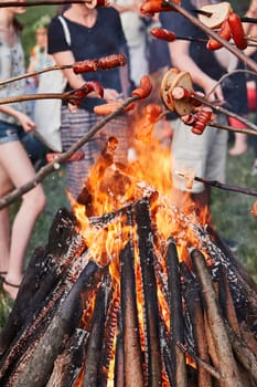 People roasting sausages and bread over a bonfire during picnic party on summer vacation day. Real people, authentic situations