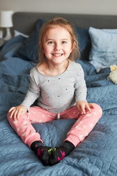 Little happy playful kid girl having fun making silly funny faces jumping on bed in bedroom in the morning at home