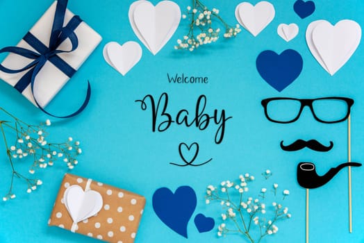 Flat Lay With English Text Welcome Baby. Blue Accessories Like Presents, Hearts, Flowers And Male Decoration Like Mustache. Flat Lay With Turquoise Paper Background.