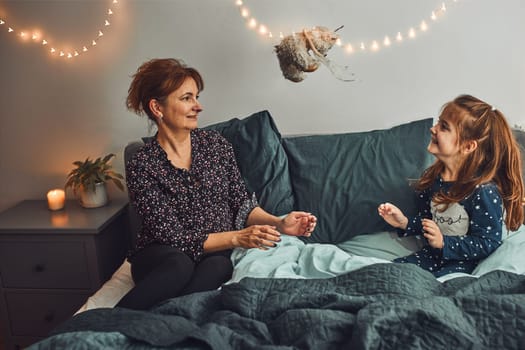 Mother playing with her little daughter in bed, having fun before going sleep. Mom throwing teddy bear to her cute daughter before bedtime