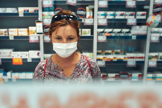 Woman shopping at pharmacy, buying medicines, wearing face mask to cover mouth and nose during pandemic coronavirus outbreak