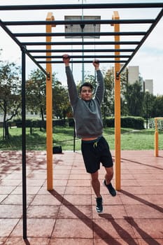 Young man bodybuilder exercising on monkey bars during his workout in a modern calisthenics street workout park. Man wearing sportswear
