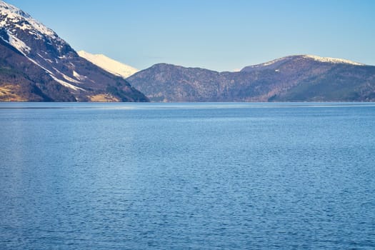 Fjord with snow covered mountains on the horizon. The water glistens in Norway. Landscape photo from the north