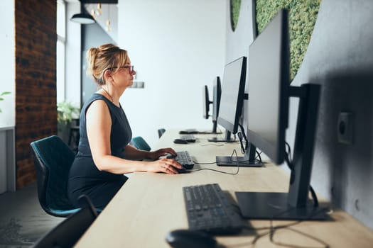 Concerned businesswoman working on computer in office. Busy woman sitting at desk at front of computer monitor. Focusing on work. Open office. Copy space right