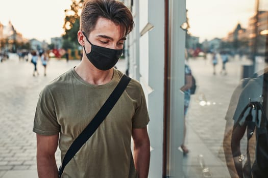 Young man walking along a store front in the city center in the evening wearing the face mask to avoid virus infection and to prevent the spread of disease in time of coronavirus