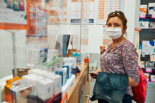 Woman shopping at pharmacy, buying medicines, wearing face mask to cover mouth and nose during pandemic coronavirus outbreak
