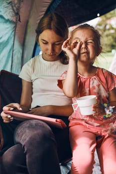 Two girls sisters spending family time in a tent on camping. Children using tablet playing games online during summer vacation