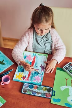Little girl preschooler painting a picture using colorful paints and crayons. Child having fun making a picture during an art class in the classroom