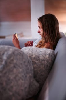 Teenage girl watching video online on smartphone sitting on sofa at home