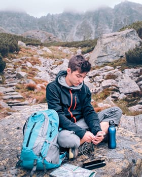 Boy resting on a rock and charging a mobile phone during trip in the Tatra Mountains