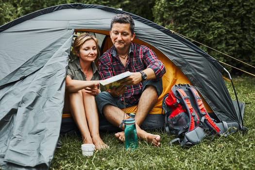 Happy couple relaxing in tent at camping during summer vacation. Man and woman planning next trip looking at map. Actively spending vacations outdoors close to nature. Concept of camp life