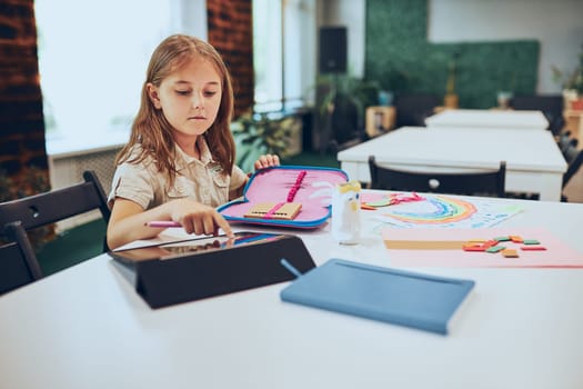 Schoolgirl using tablet. Child doing homework sitting at desk in afterschool club. Girl drawing pictures on tablet. Learning using technology. Back to school
