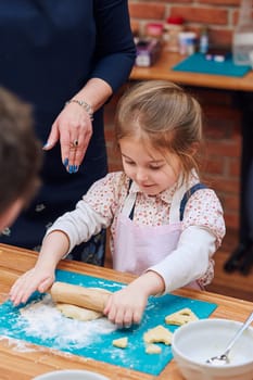Little girl rolling the dough with her mom's help for the cookies. Cutting the dough to heart shapes. Kid taking part in baking workshop. Baking classes for children, aspiring little chefs. Learning to cook. Combining and stirring prepared ingredients. Real people, authentic situations